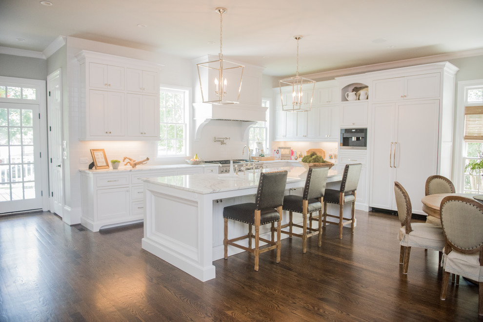 Large country l-shaped kitchen in Atlanta with a farmhouse sink, beaded inset cabinets, white cabinets, marble benchtops, white splashback, ceramic splashback, panelled appliances, dark hardwood floors and with island.