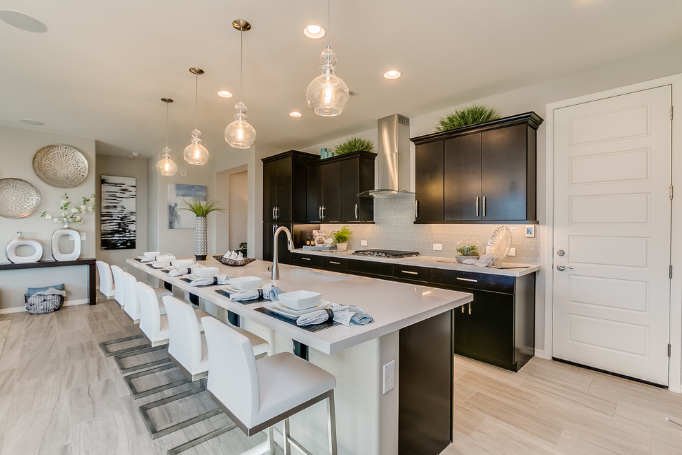 Photo of a large contemporary l-shaped eat-in kitchen in Phoenix with a double-bowl sink, flat-panel cabinets, black cabinets, solid surface benchtops, grey splashback, subway tile splashback, stainless steel appliances, ceramic floors, with island and beige floor.