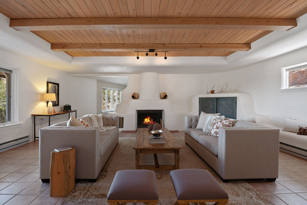 Пример оригинального дизайна: большая открытая гостиная комната в стиле фьюжн с белыми стенами, полом из керамической плитки, стандартным камином, фасадом камина из штукатурки, скрытым телевизором, коричневым полом и балками на потолке