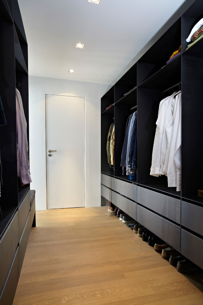 Photo of a contemporary men's walk-in wardrobe in Amsterdam with flat-panel cabinets, black cabinets, light hardwood floors and beige floor.