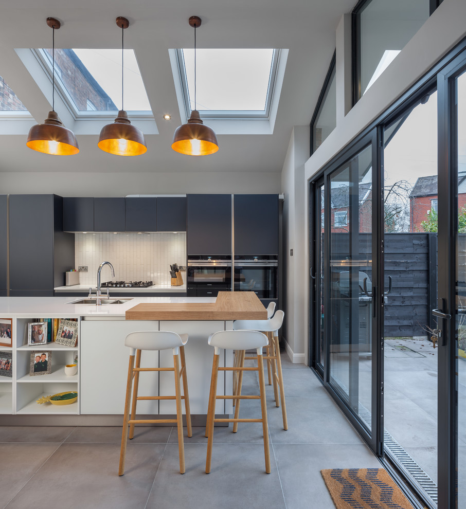 Photo of a mid-sized contemporary galley eat-in kitchen in Manchester with flat-panel cabinets, grey cabinets, wood benchtops, white splashback, subway tile splashback, cement tiles, with island, grey floor and a double-bowl sink.