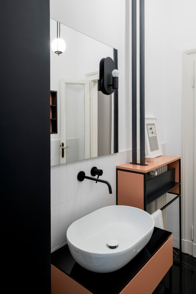 This is an example of a mid-sized scandinavian 3/4 bathroom in Milan with shaker cabinets, an open shower, a wall-mount toilet, white tile, ceramic tile, white walls, porcelain floors, a vessel sink, glass benchtops, black floor, an open shower, black benchtops, a niche, a single vanity and a freestanding vanity.