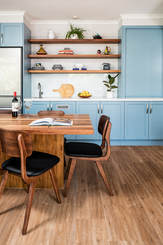 This is an example of a large transitional eat-in kitchen in Melbourne with a double-bowl sink, shaker cabinets, blue cabinets, quartz benchtops, white splashback, glass sheet splashback, black appliances, medium hardwood floors, with island, brown floor and white benchtop.