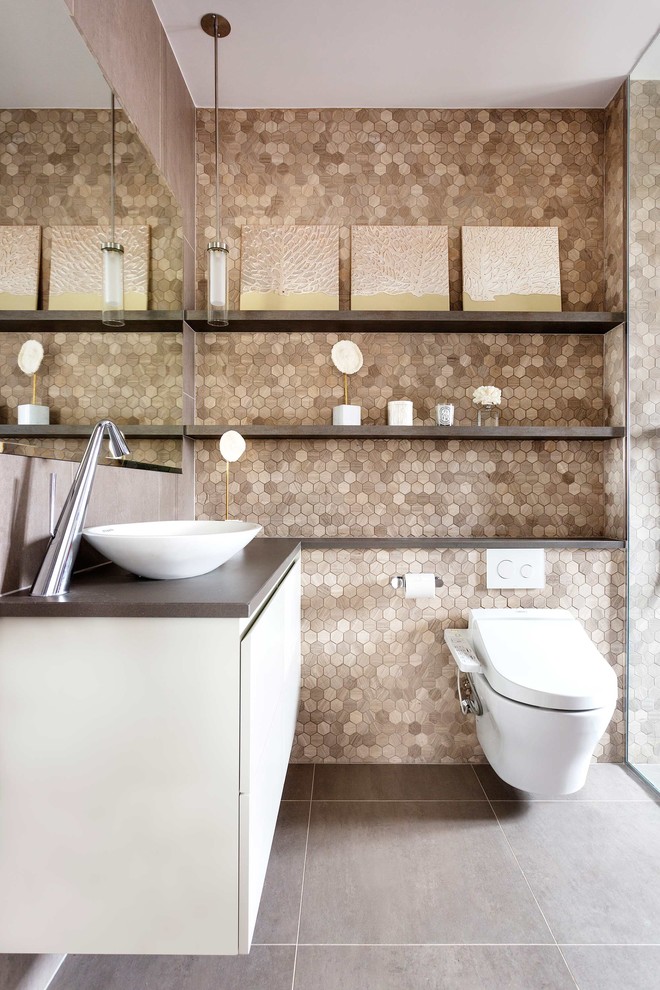This is an example of a mid-sized contemporary bathroom in London with flat-panel cabinets, white cabinets, a wall-mount toilet, beige tile, brown walls, a vessel sink, grey floor and black benchtops.