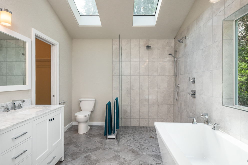 This is an example of a large contemporary master bathroom in Seattle with shaker cabinets, white cabinets, a freestanding tub, a curbless shower, a two-piece toilet, gray tile, porcelain tile, grey walls, porcelain floors, an undermount sink, marble benchtops, grey floor, an open shower and white benchtops.