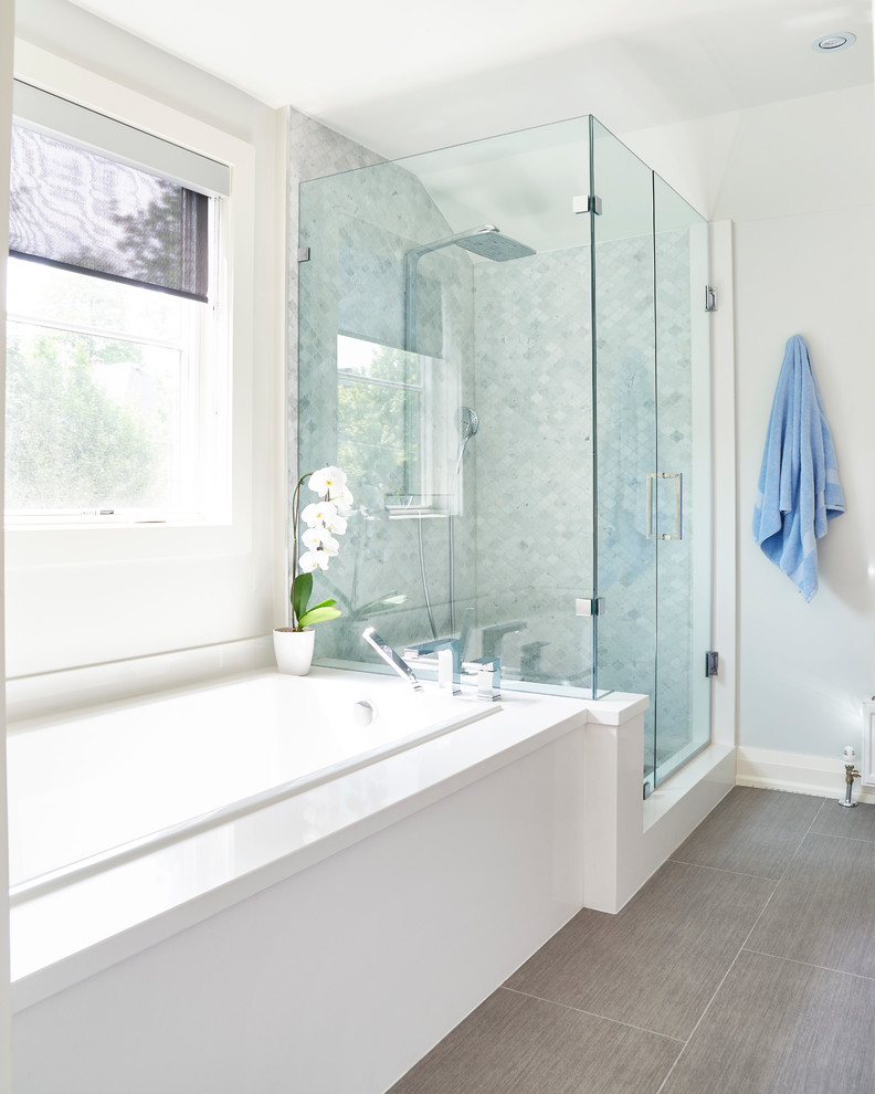 Inspiration for a small transitional master bathroom in Toronto with shaker cabinets, medium wood cabinets, a drop-in tub, a shower/bathtub combo, a two-piece toilet, gray tile, stone tile, grey walls, ceramic floors, an undermount sink and solid surface benchtops.