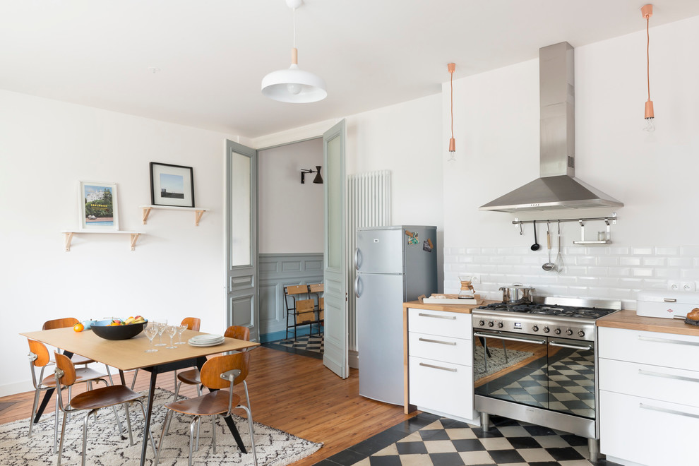 Design ideas for a large scandinavian l-shaped eat-in kitchen in Bordeaux with flat-panel cabinets, white cabinets, wood benchtops, white splashback, subway tile splashback, stainless steel appliances and no island.