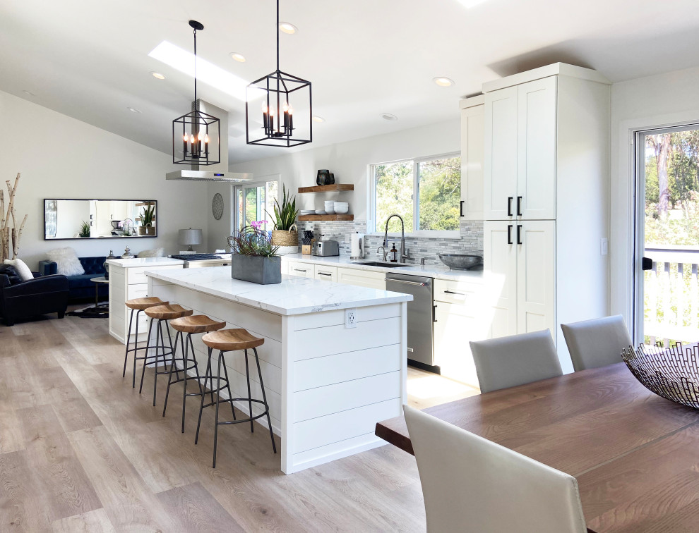 Inspiration for a mid-sized transitional l-shaped vinyl floor, brown floor and vaulted ceiling eat-in kitchen remodel with an undermount sink, shaker cabinets, white cabinets, quartz countertops, multicolored backsplash, mosaic tile backsplash, stainless steel appliances, an island and white countertops