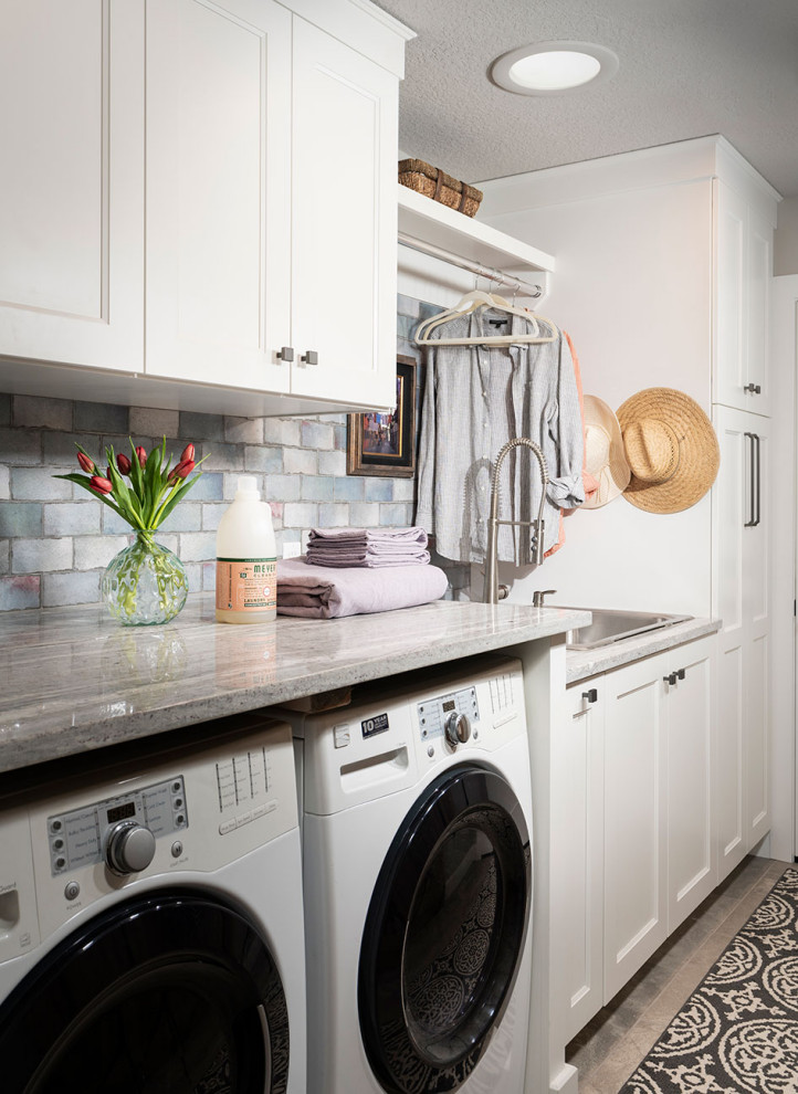 This is an example of a small traditional single-wall dedicated laundry room in Other with a drop-in sink, white cabinets, granite benchtops, blue splashback, subway tile splashback, ceramic floors, a side-by-side washer and dryer, grey floor and grey benchtop.