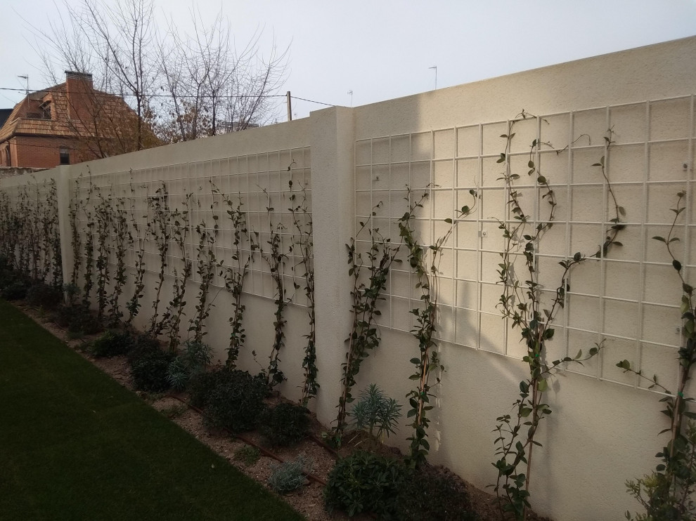 This is an example of a medium sized modern back driveway partial sun pergola for winter in Madrid with gravel and a stone fence.