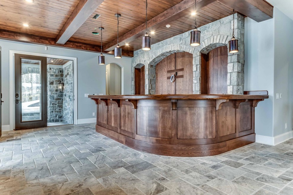 This is an example of a mid-sized country seated home bar in Cleveland with recessed-panel cabinets, dark wood cabinets, wood benchtops, brown splashback, timber splashback, limestone floors and grey floor.