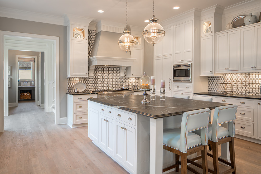 Example of a large transitional u-shaped light wood floor and brown floor kitchen design in Cincinnati with recessed-panel cabinets, white cabinets, marble countertops, multicolored backsplash, paneled appliances, an island and black countertops