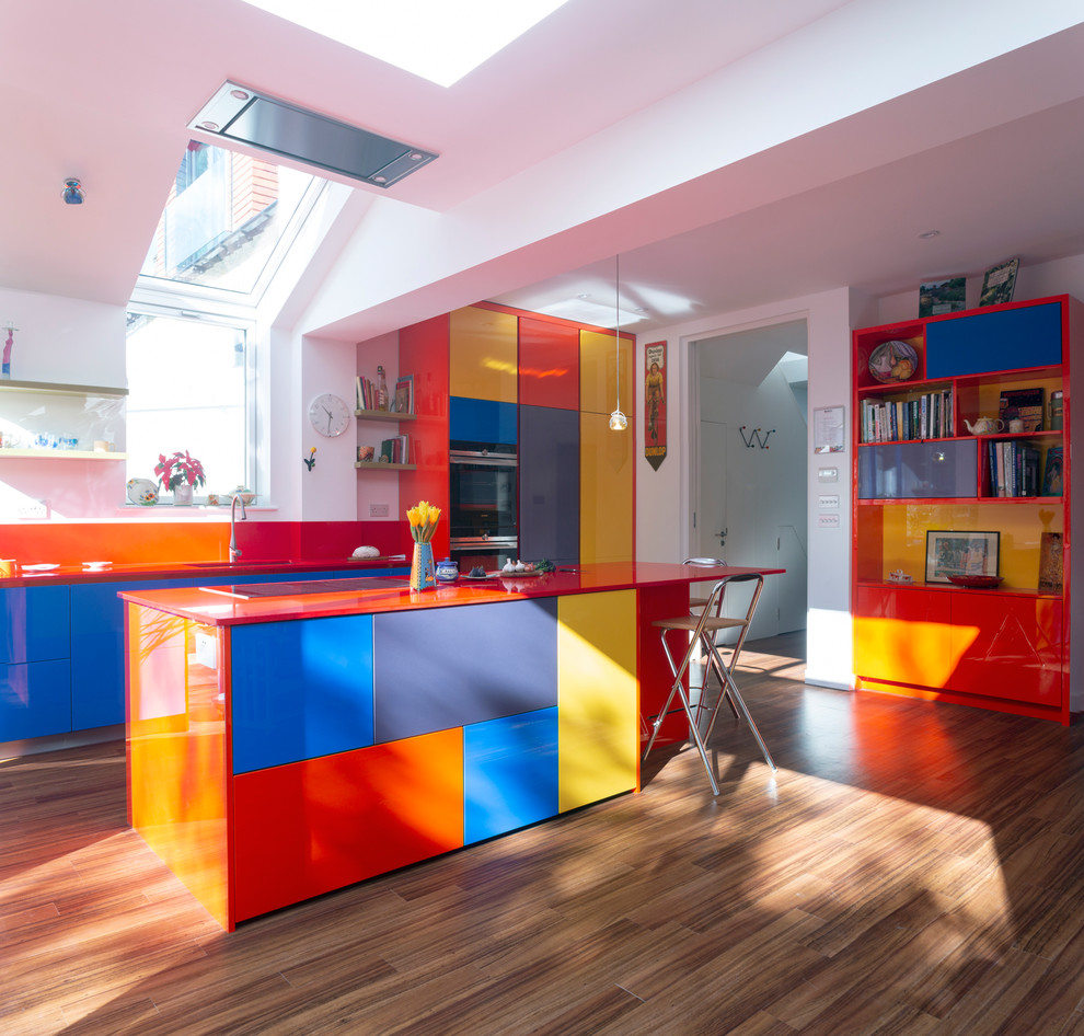 Large contemporary galley kitchen in London with an integrated sink, flat-panel cabinets, laminate benchtops, stainless steel appliances, brown floor, red benchtop, red cabinets, red splashback and with island.