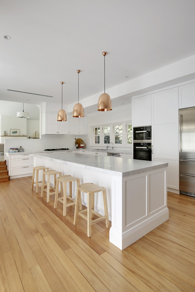 Photo of a large traditional l-shaped eat-in kitchen in Sydney with a double-bowl sink, shaker cabinets, white cabinets, marble benchtops, white splashback, ceramic splashback, stainless steel appliances, light hardwood floors, with island and yellow floor.