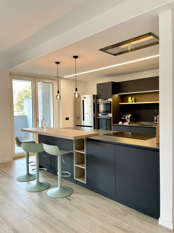 Photo of a large contemporary galley open plan kitchen in Milan with an undermount sink, flat-panel cabinets, black cabinets, solid surface benchtops, black splashback, stainless steel appliances, porcelain floors, a peninsula, beige floor, grey benchtop and recessed.