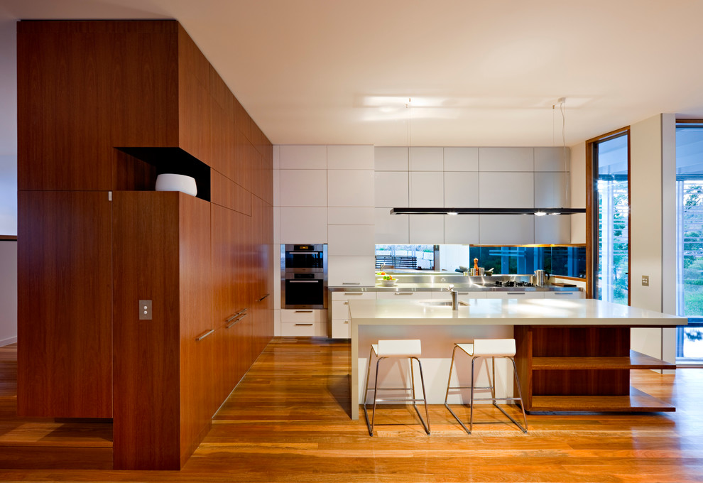Photo of a contemporary galley kitchen in Brisbane with flat-panel cabinets, white cabinets, medium hardwood floors and with island.