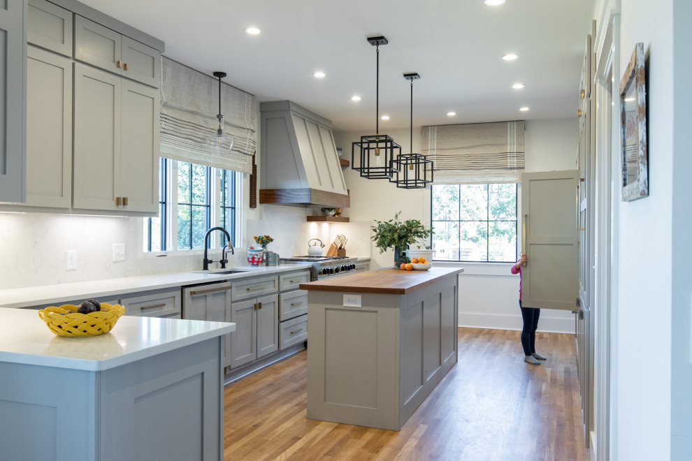Inspiration for a transitional u-shaped medium tone wood floor and brown floor kitchen remodel in Atlanta with an undermount sink, shaker cabinets, gray cabinets, white backsplash, stone slab backsplash, paneled appliances, a peninsula and white countertops