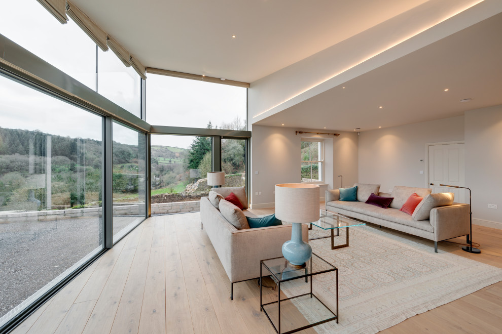 This is an example of a large contemporary open concept living room in Devon with beige walls and light hardwood floors.