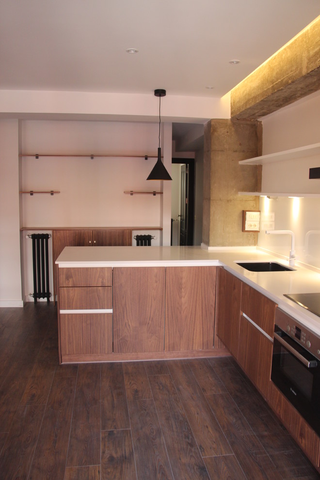 This is an example of a small industrial l-shaped open plan kitchen in Madrid with an undermount sink, flat-panel cabinets, medium wood cabinets, quartz benchtops, white splashback, window splashback, black appliances, dark hardwood floors and a peninsula.