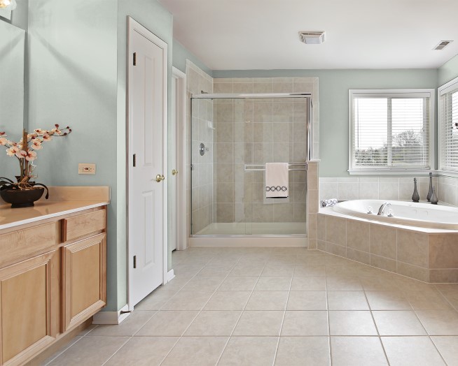 Design ideas for a mid-sized contemporary master bathroom in DC Metro with beige tile, green walls, ceramic floors, recessed-panel cabinets, light wood cabinets, a drop-in tub, a corner shower, porcelain tile, laminate benchtops, beige floor, a sliding shower screen and white benchtops.