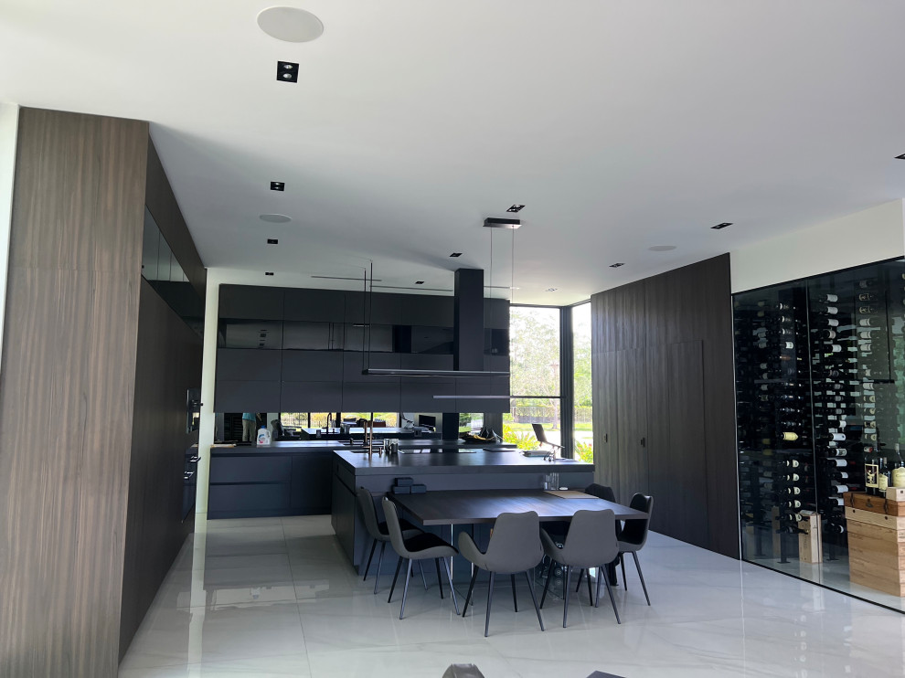 Design ideas for an expansive modern u-shaped eat-in kitchen in Miami with an undermount sink, flat-panel cabinets, brown cabinets, quartz benchtops, black splashback, glass sheet splashback, black appliances, with island and black benchtop.