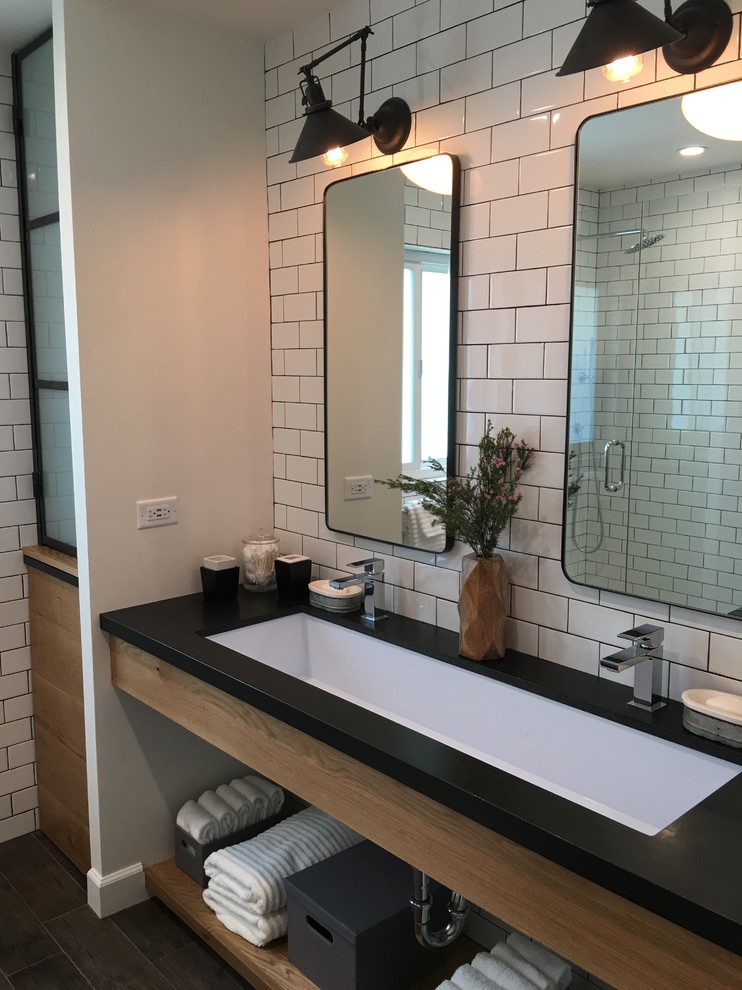 Photo of a mid-sized industrial kids bathroom in Los Angeles with open cabinets, medium wood cabinets, an alcove shower, a one-piece toilet, white tile, subway tile, white walls, a trough sink, granite benchtops, porcelain floors and brown floor.