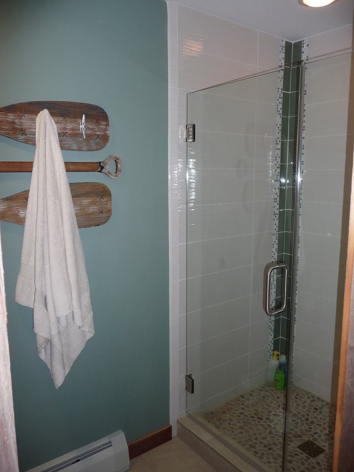 Photo of a mid-sized beach style 3/4 bathroom in Milwaukee with raised-panel cabinets, white cabinets, an alcove shower, a two-piece toilet, white tile, porcelain tile, blue walls, porcelain floors, an undermount sink and quartzite benchtops.