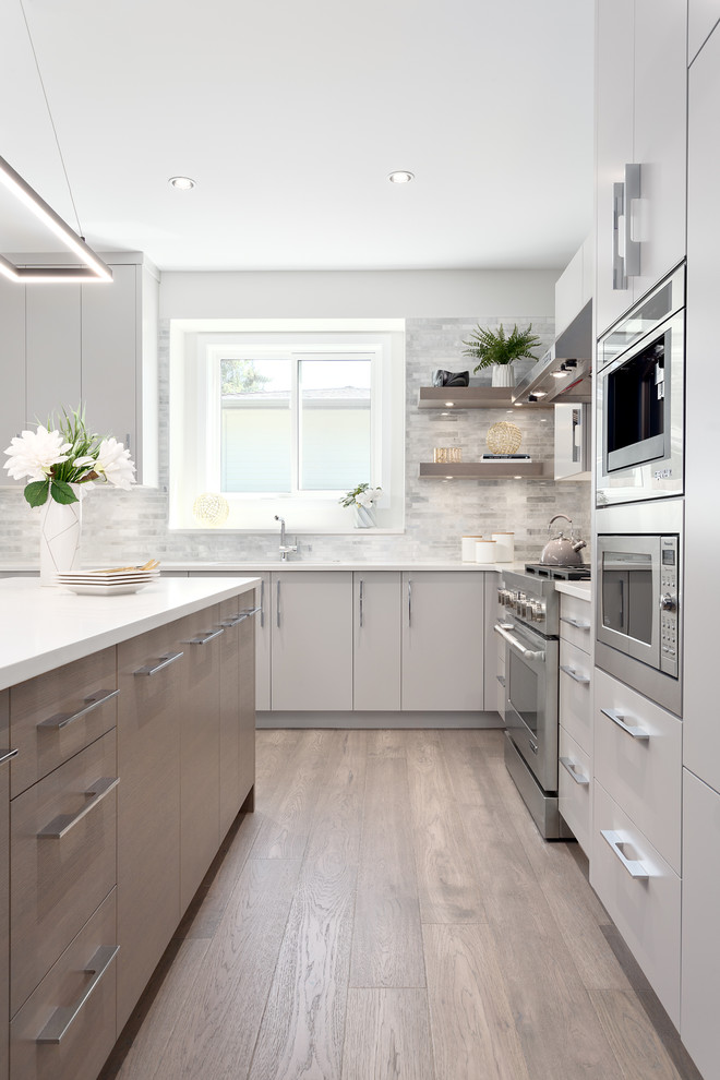 Photo of a mid-sized contemporary l-shaped open plan kitchen in Vancouver with a double-bowl sink, flat-panel cabinets, grey cabinets, stone tile splashback, panelled appliances, medium hardwood floors, with island, brown floor, white benchtop, solid surface benchtops and white splashback.