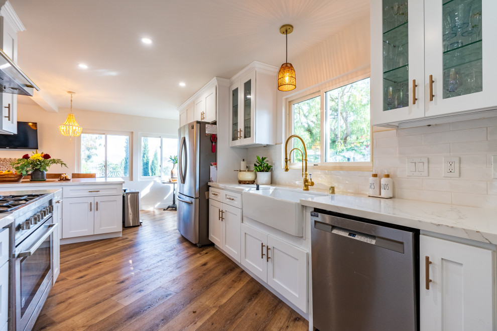 Mid-sized eclectic galley eat-in kitchen in Los Angeles with a farmhouse sink, beaded inset cabinets, white cabinets, marble benchtops, grey splashback, marble splashback, stainless steel appliances, plywood floors, with island, brown floor and white benchtop.
