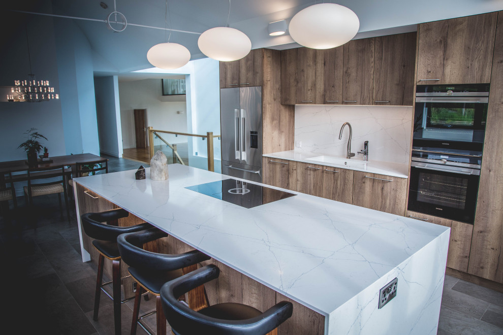 This is an example of a large contemporary single-wall open plan kitchen in Devon with an integrated sink, flat-panel cabinets, medium wood cabinets, quartzite benchtops, stainless steel appliances, with island, white benchtop and vaulted.