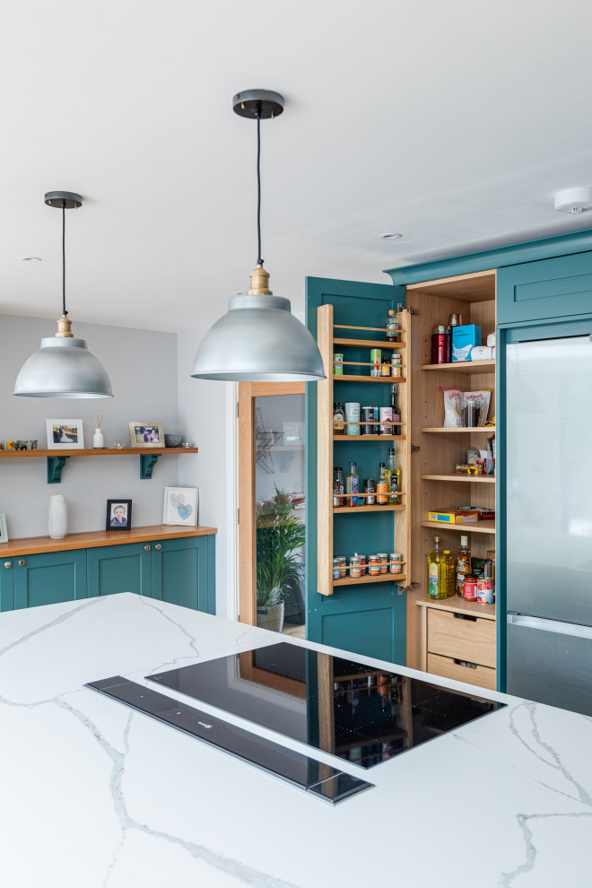 This is an example of a large traditional l-shaped open plan kitchen in Hertfordshire with a built-in sink, shaker cabinets, green cabinets, quartz worktops, integrated appliances, laminate floors, an island and white worktops.