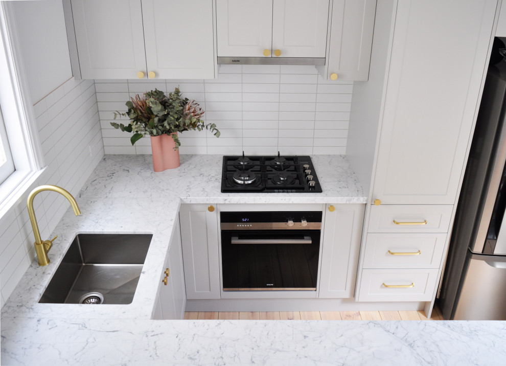 Modern inredning av ett mellanstort flerfärgad flerfärgat kök, med en enkel diskho, vita skåp, marmorbänkskiva, vitt stänkskydd, stänkskydd i tunnelbanekakel, rostfria vitvaror och mellanmörkt trägolv