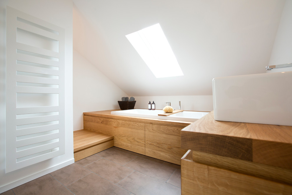 Mid-sized contemporary bathroom in Frankfurt with a vessel sink, flat-panel cabinets, medium wood cabinets, wood benchtops, a drop-in tub, brown tile, white walls and a two-piece toilet.