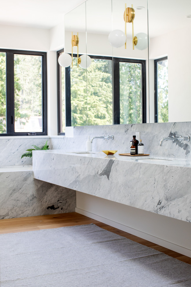 Cette photo montre une salle de bain moderne avec une baignoire encastrée, un carrelage gris, des dalles de pierre, un mur blanc, un sol en bois brun, un lavabo encastré, un sol marron, un plan de toilette gris et meuble double vasque.
