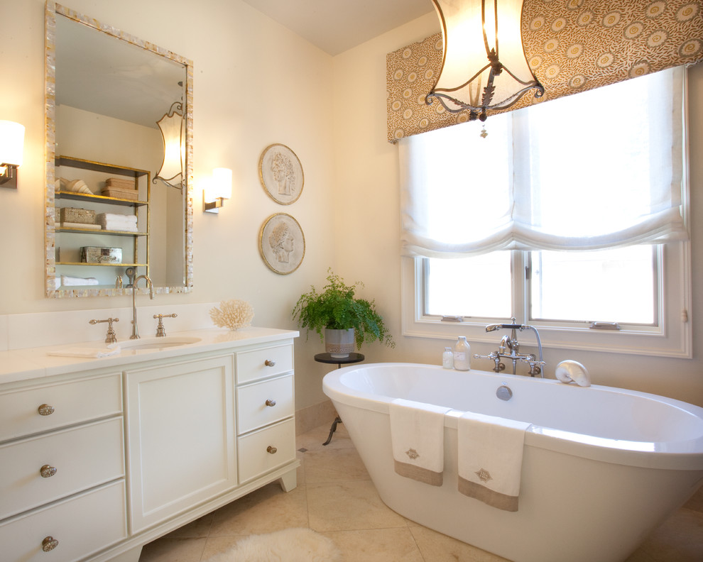 This is an example of a transitional master bathroom in Sacramento with furniture-like cabinets, white cabinets, a freestanding tub, beige tile, stone tile, white walls, limestone floors, an undermount sink and marble benchtops.