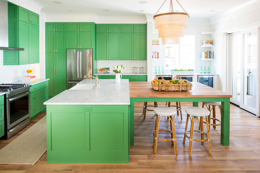 Inspiration for a large beach style l-shaped open plan kitchen in Minneapolis with a farmhouse sink, shaker cabinets, green cabinets, marble benchtops, white splashback, subway tile splashback, stainless steel appliances, light hardwood floors, multiple islands and brown floor.
