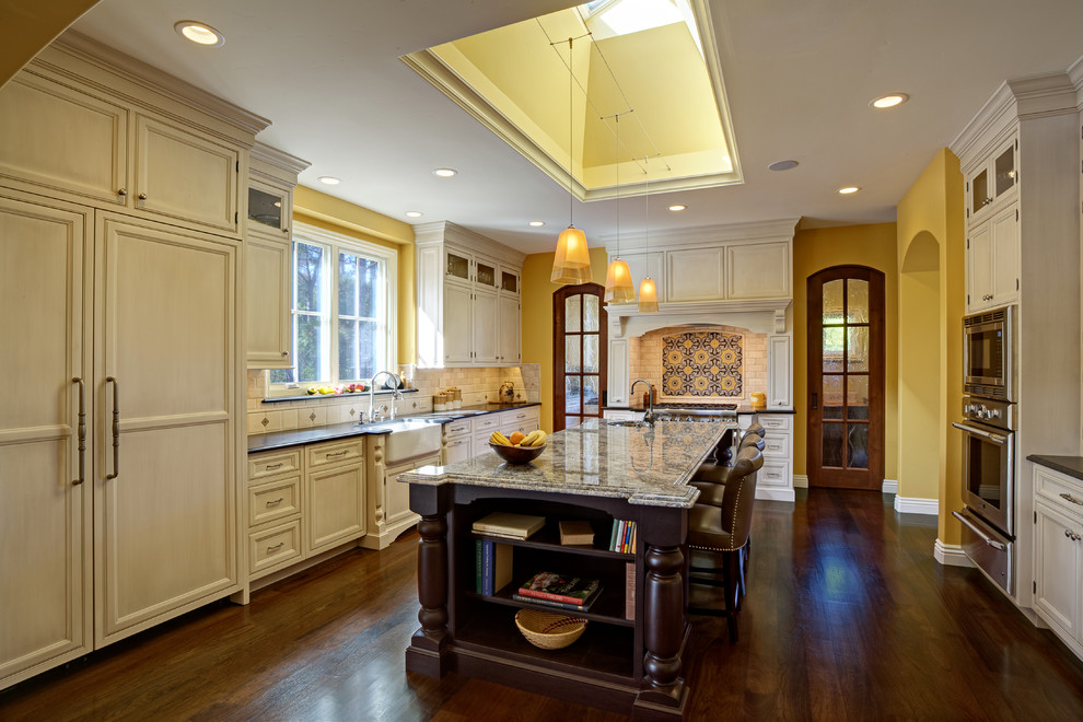 Example of a large transitional u-shaped dark wood floor open concept kitchen design in San Francisco with a farmhouse sink, beaded inset cabinets, white cabinets, granite countertops, beige backsplash, stone tile backsplash, paneled appliances and an island