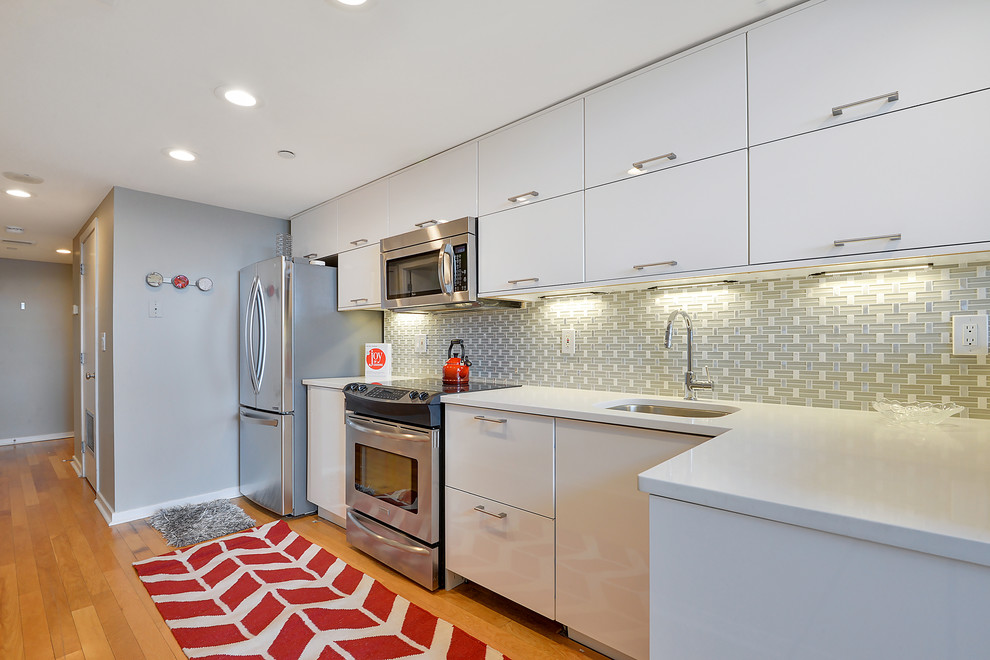 Photo of a mid-sized contemporary l-shaped separate kitchen in New York with an undermount sink, flat-panel cabinets, white cabinets, quartz benchtops, multi-coloured splashback, ceramic splashback, stainless steel appliances, light hardwood floors and a peninsula.