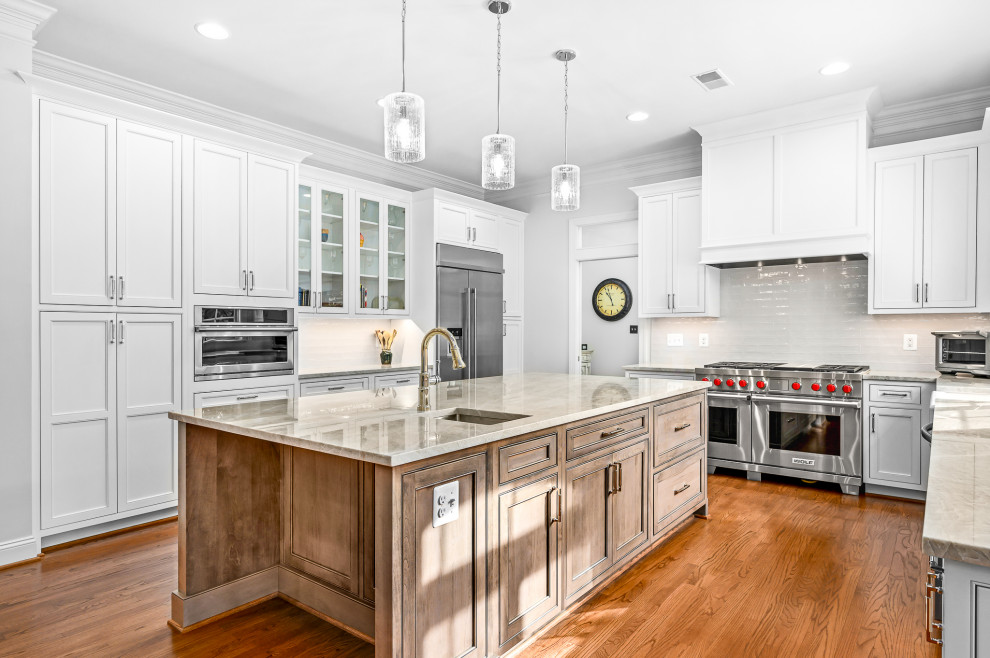 Traditional eat-in kitchen in DC Metro with a farmhouse sink, beaded inset cabinets, white cabinets, quartzite benchtops, white splashback, ceramic splashback, stainless steel appliances, medium hardwood floors, with island, brown floor and beige benchtop.