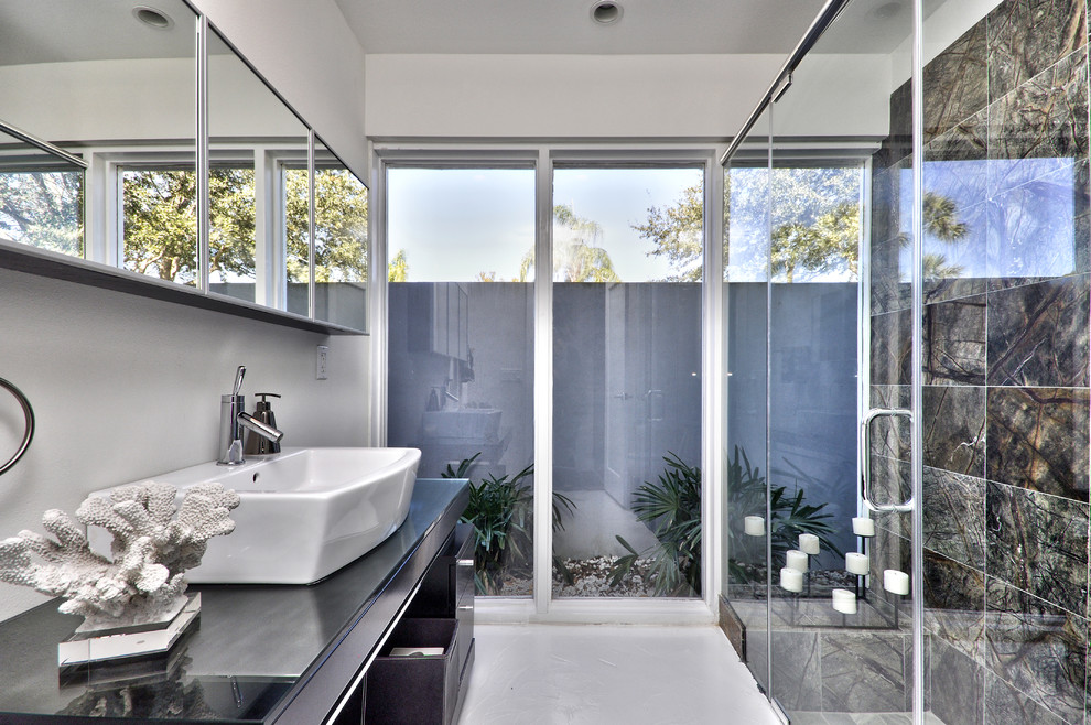 Design ideas for a large contemporary 3/4 bathroom in Tampa with flat-panel cabinets, dark wood cabinets, a curbless shower, a two-piece toilet, multi-coloured tile, stone tile, concrete floors, a vessel sink, glass benchtops and grey walls.