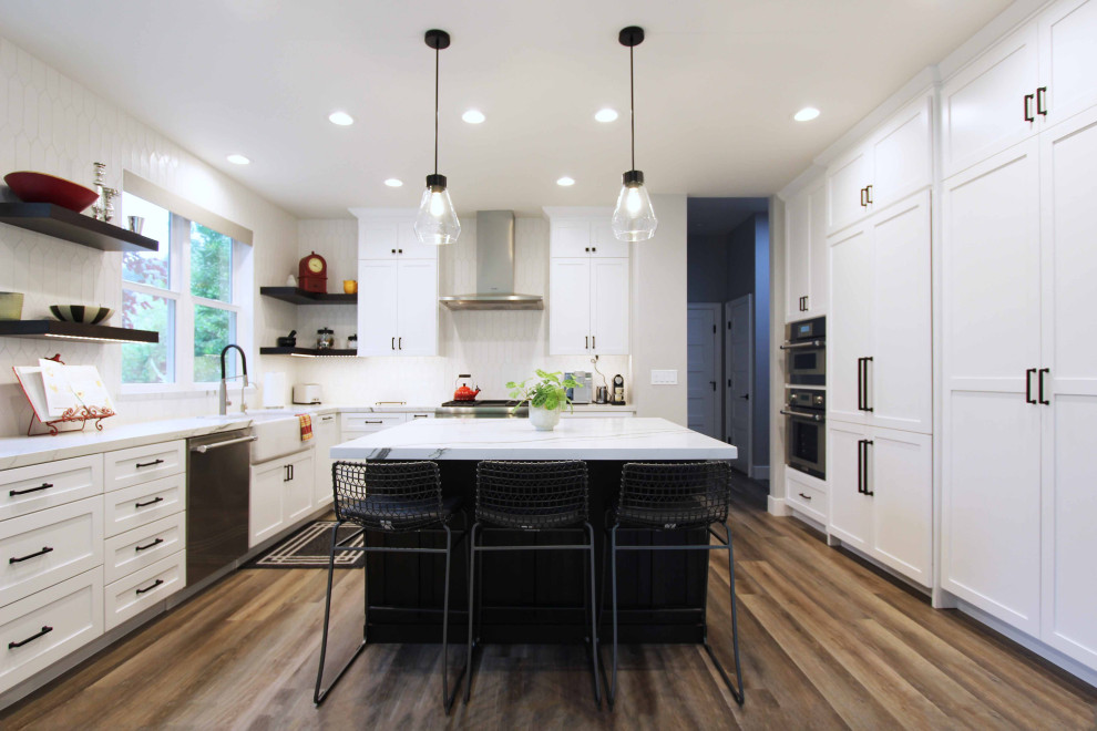 Large transitional l-shaped vinyl floor and brown floor open concept kitchen photo with a farmhouse sink, shaker cabinets, white cabinets, quartz countertops, white backsplash, ceramic backsplash, stainless steel appliances, an island and white countertops