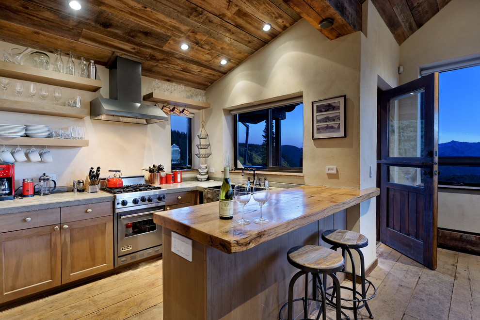 Example of a mountain style light wood floor kitchen design in Denver with a farmhouse sink, recessed-panel cabinets, light wood cabinets, stainless steel appliances, a peninsula and gray countertops