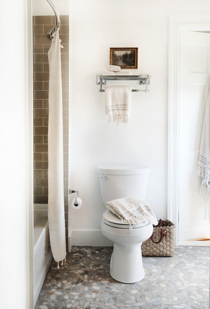 Photo of a mid-sized beach style 3/4 bathroom in New York with an undermount sink, distressed cabinets, marble benchtops, an alcove tub, a shower/bathtub combo, a one-piece toilet, multi-coloured tile, pebble tile, white walls and pebble tile floors.