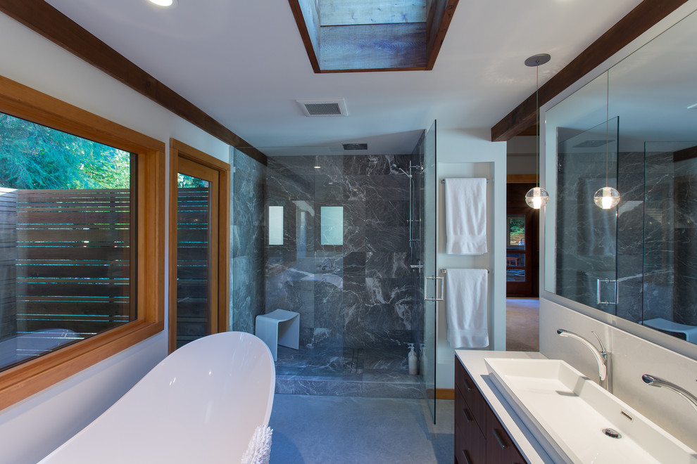 Inspiration for a mid-sized midcentury master bathroom in Vancouver with a trough sink, flat-panel cabinets, dark wood cabinets, a freestanding tub, an alcove shower, gray tile, engineered quartz benchtops, a hinged shower door and white benchtops.