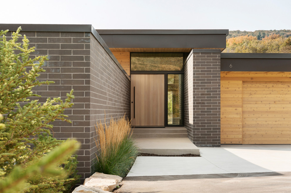 Photo of a modern front door in Salt Lake City with white walls, concrete floors, a pivot front door, a light wood front door, grey floor, wood and brick walls.