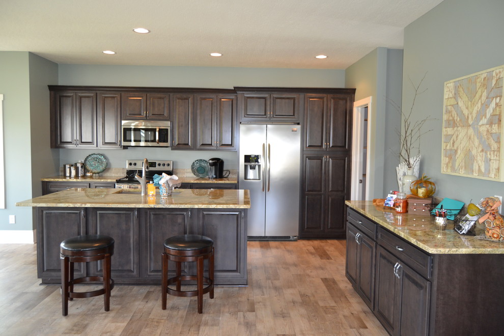 Large transitional l-shaped vinyl floor and beige floor eat-in kitchen photo in Cleveland with an undermount sink, raised-panel cabinets, dark wood cabinets, granite countertops, gray backsplash, ceramic backsplash, stainless steel appliances and an island