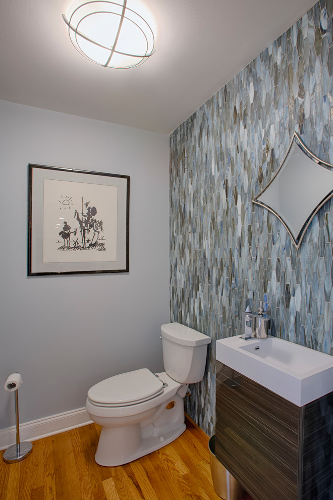 Photo of a small contemporary powder room in Nashville with flat-panel cabinets, dark wood cabinets, a two-piece toilet, multi-coloured tile, glass tile, blue walls, medium hardwood floors, an integrated sink, engineered quartz benchtops, brown floor and white benchtops.