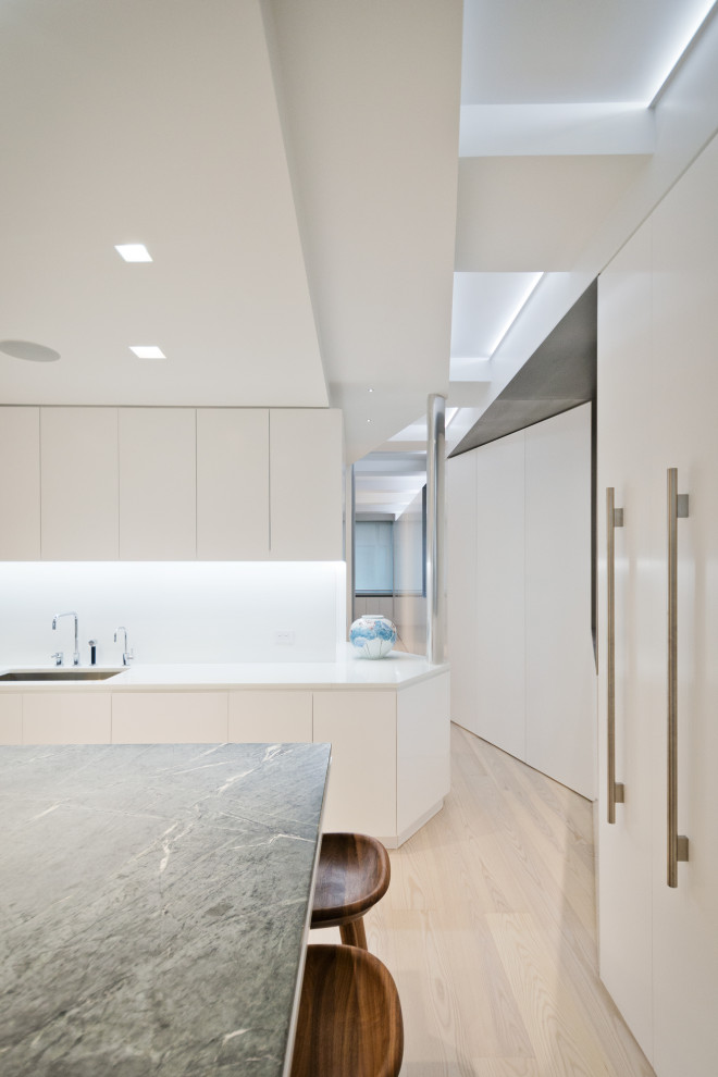 Modern u-shaped separate kitchen in New York with an undermount sink, flat-panel cabinets, white cabinets, marble benchtops, white splashback, stone slab splashback, stainless steel appliances, light hardwood floors, with island and green benchtop.