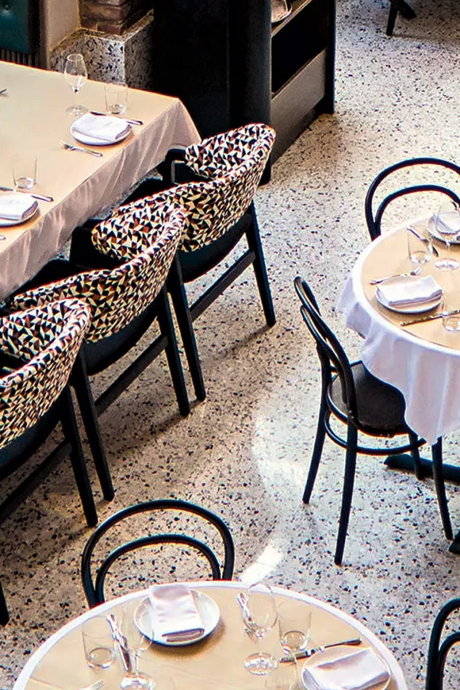 На фото: огромная кухня с обеденным столом, столешницей терраццо, бетонным полом, островом и белым полом
