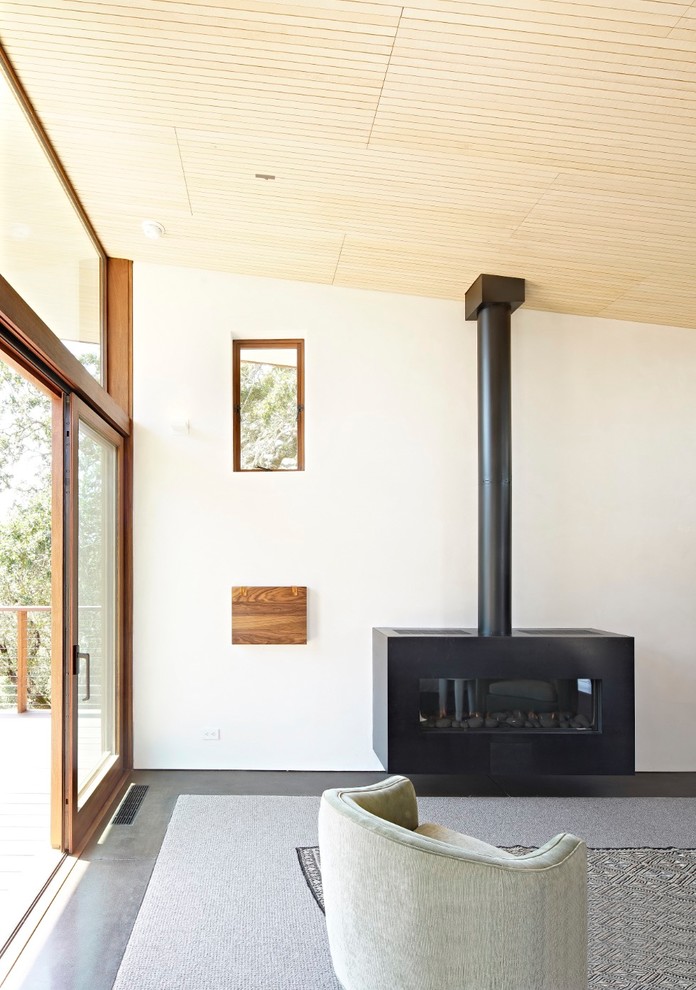 Photo of a large country master bedroom in San Francisco with white walls, concrete floors, a wood stove, a metal fireplace surround and grey floor.